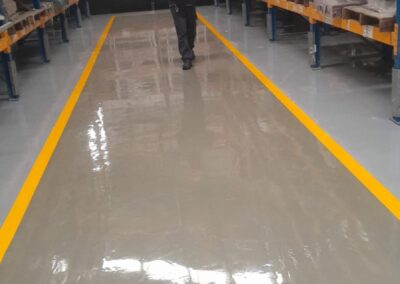 Piso epóxico multicapa brillante entre racks de taller industrial, aplicado por GSA Ingeniería