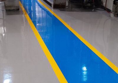 Franja azul con borde amarillo sobre piso epóxico multicapa instalado por GSA Ingeniería