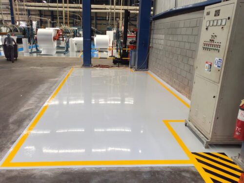 Piso conductivo gris con demarcación amarilla junto a tablero eléctrico, sistema Sikafloor aplicado por GSA Ingeniería